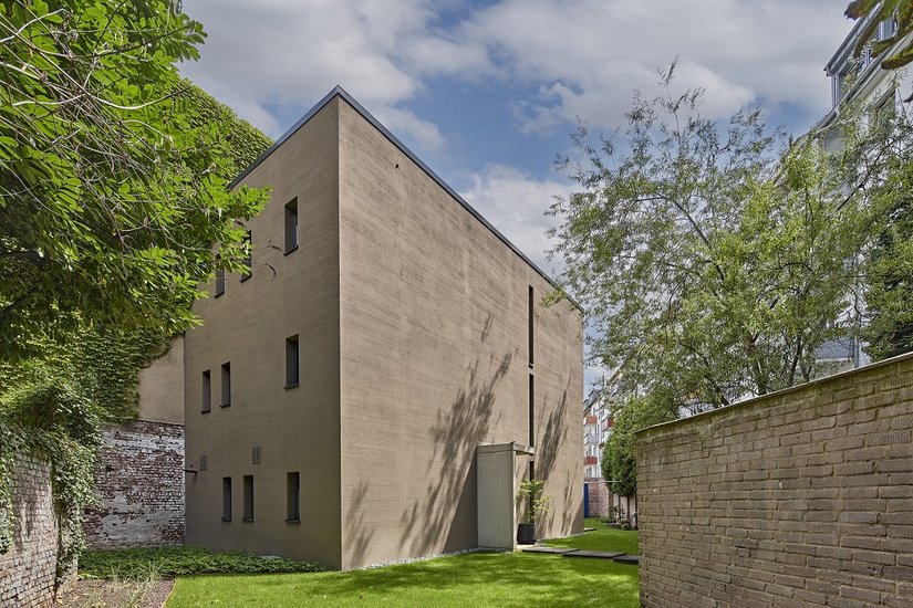 Su di un tortuoso “terreno residuo” nel centro della città è stato risolto in modo esemplare l'onnipresente problema dello spazio e degli alloggi. Sul lato ovest, ben proporzionato e monolitico, che presenta solo un elemento porta e fessure luminose, la decorazione della facciata svolge il ruolo principale.