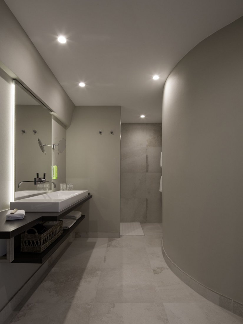 I bagni, eleganti e chiari, offrono il massimo comfort grazie all'ampia doccia a filo pavimento con funzione rainshower, agli specchi alti fino al soffitto e ai termoarredi per asciugamani.