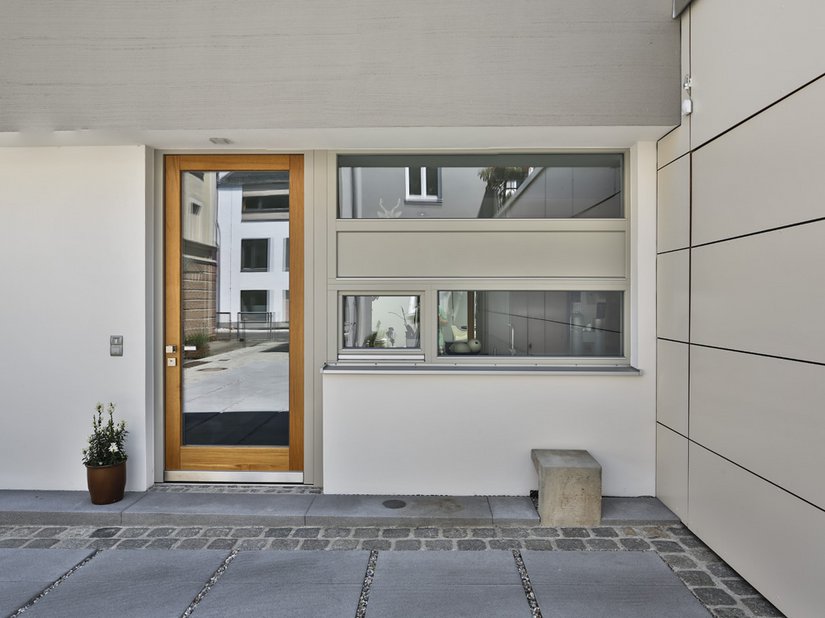 Il legno chiaro della porta dell'edificio spezza nettamente l'uniformità del grigio.