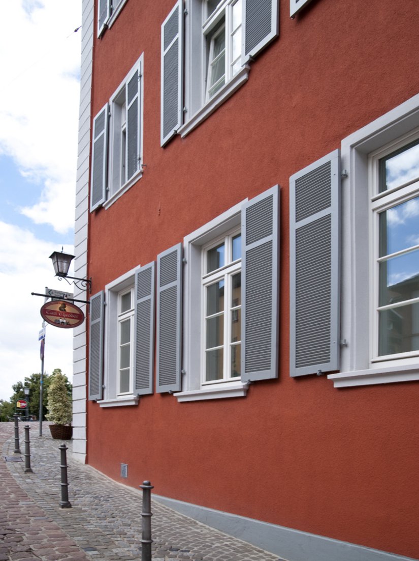 Imposte grigie e finestre bianche danno ritmo alla facciata rossa.