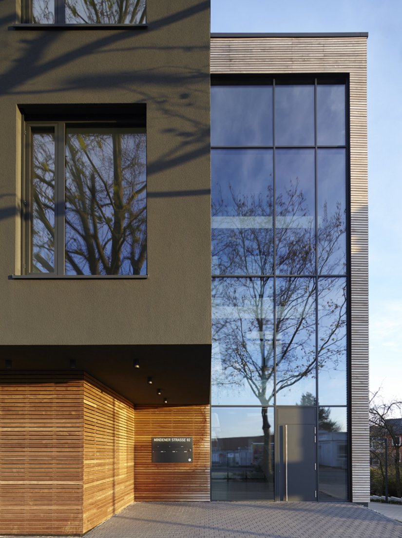 La struttura in filigrana delle lamelle di legno orizzontali alleggerisce la costruzione in cemento armato e crea un piacevole contrasto con la facciata intonacata monocromatica dalla tinta scura.